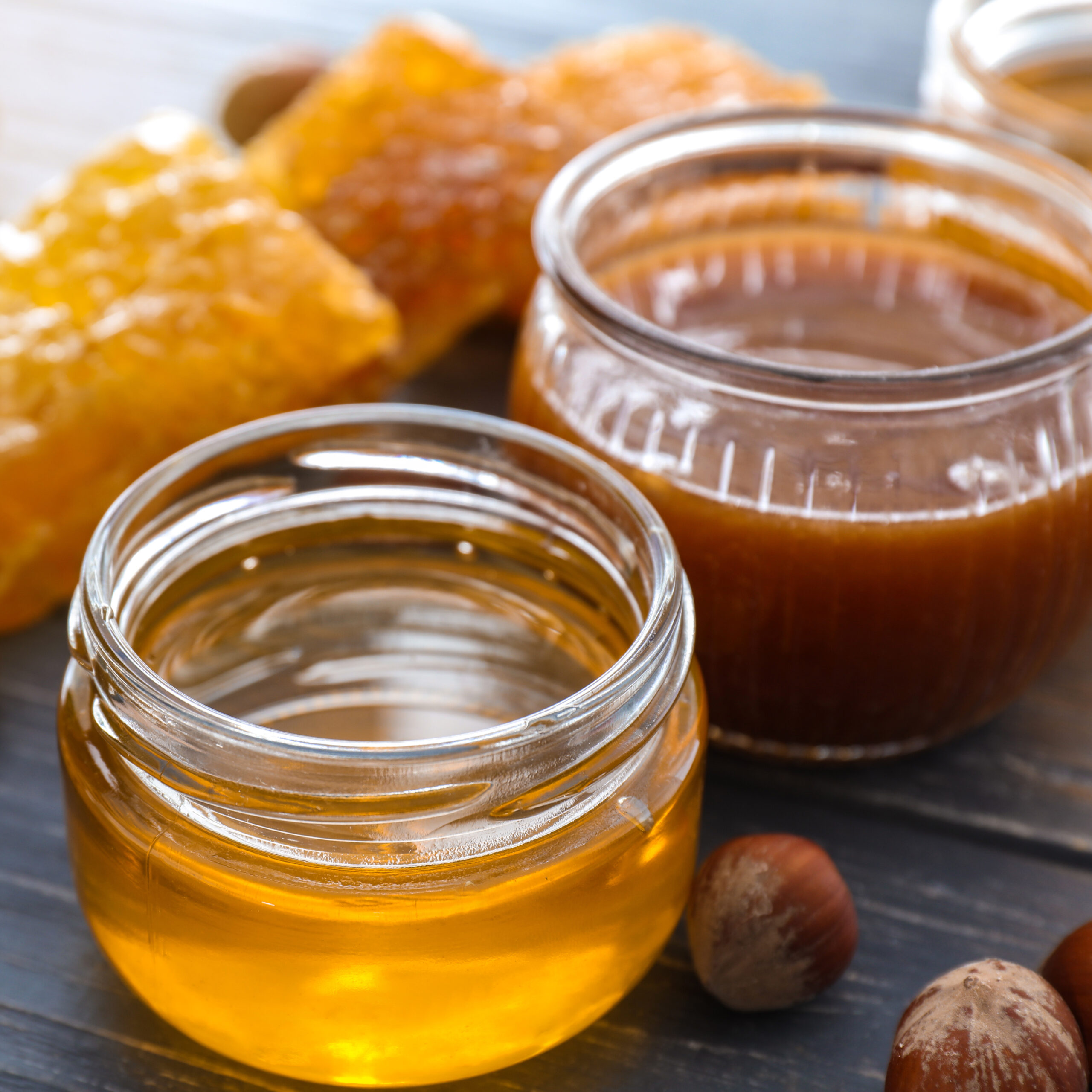 Full jars of honey with honeycomb on wooden table, closeup