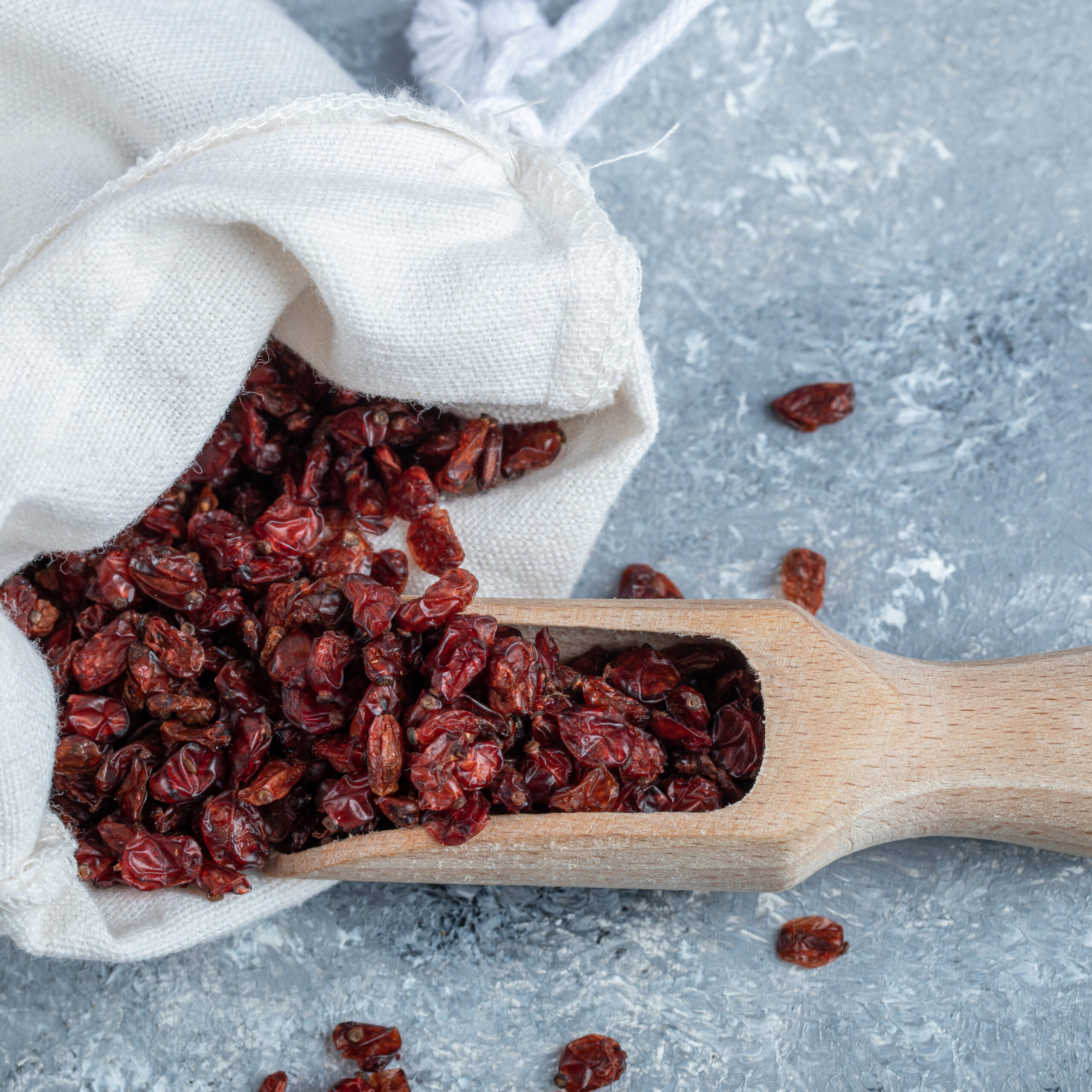 A wooden spoon full of dried cranberries on marble surface