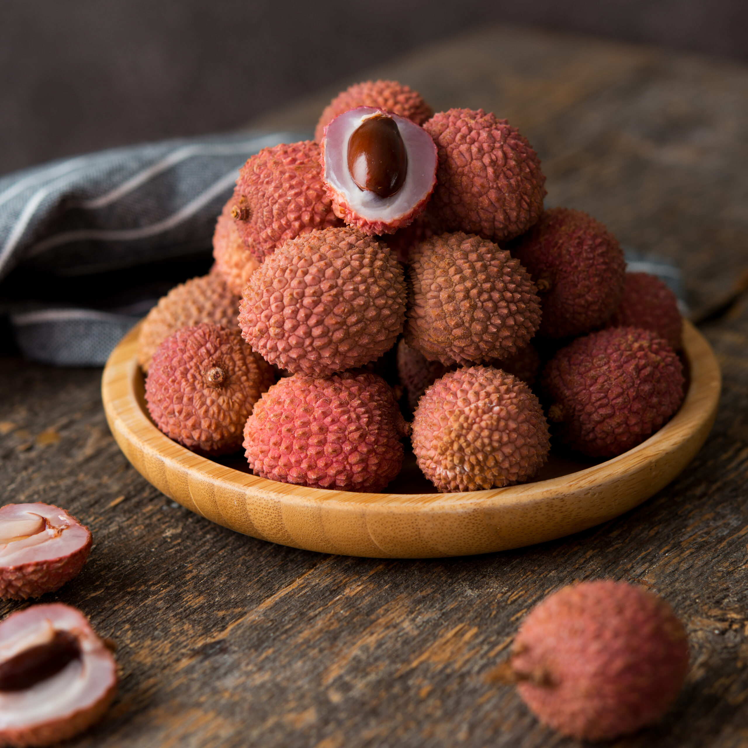 Ripe lychee berries in a plate on a wooden table, selective focu